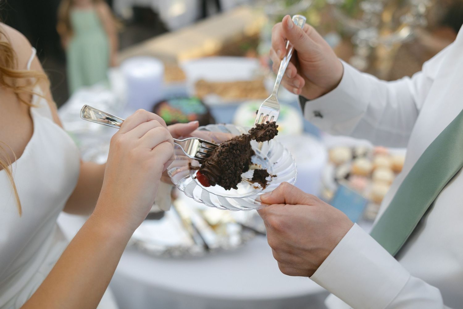 Bride and groom cutting a chocolate wedding cake together at an outdoor reception table.
