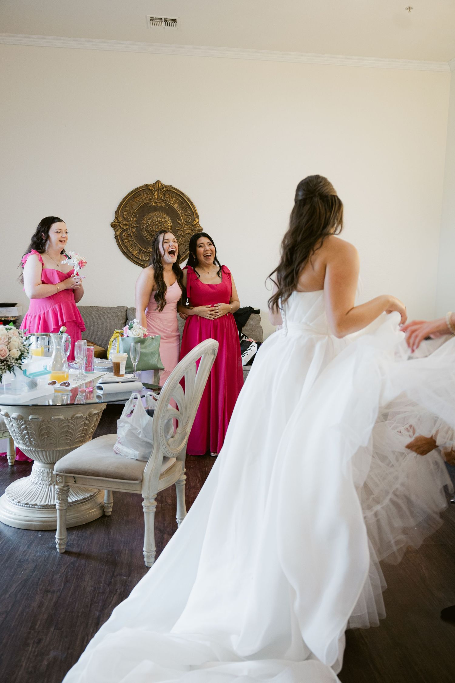 Bridesmaids in pink dresses gather around a bride in a white gown during wedding preparations.