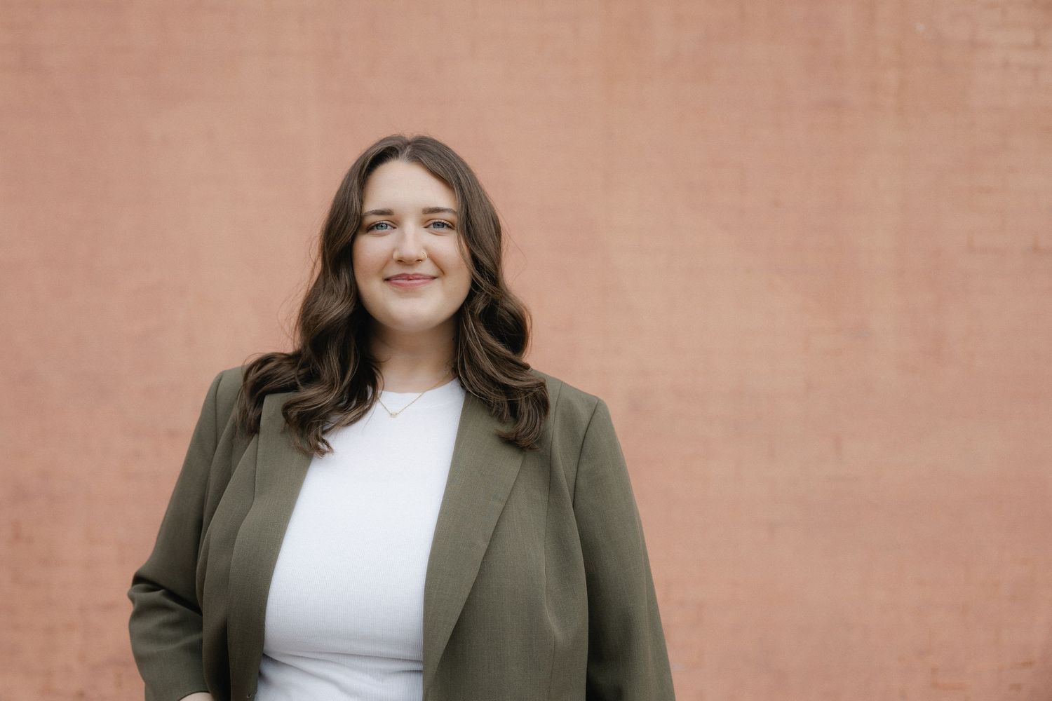 Professional wearing an olive blazer and white top poses against a coral-colored wall in multiple cropped headshots.