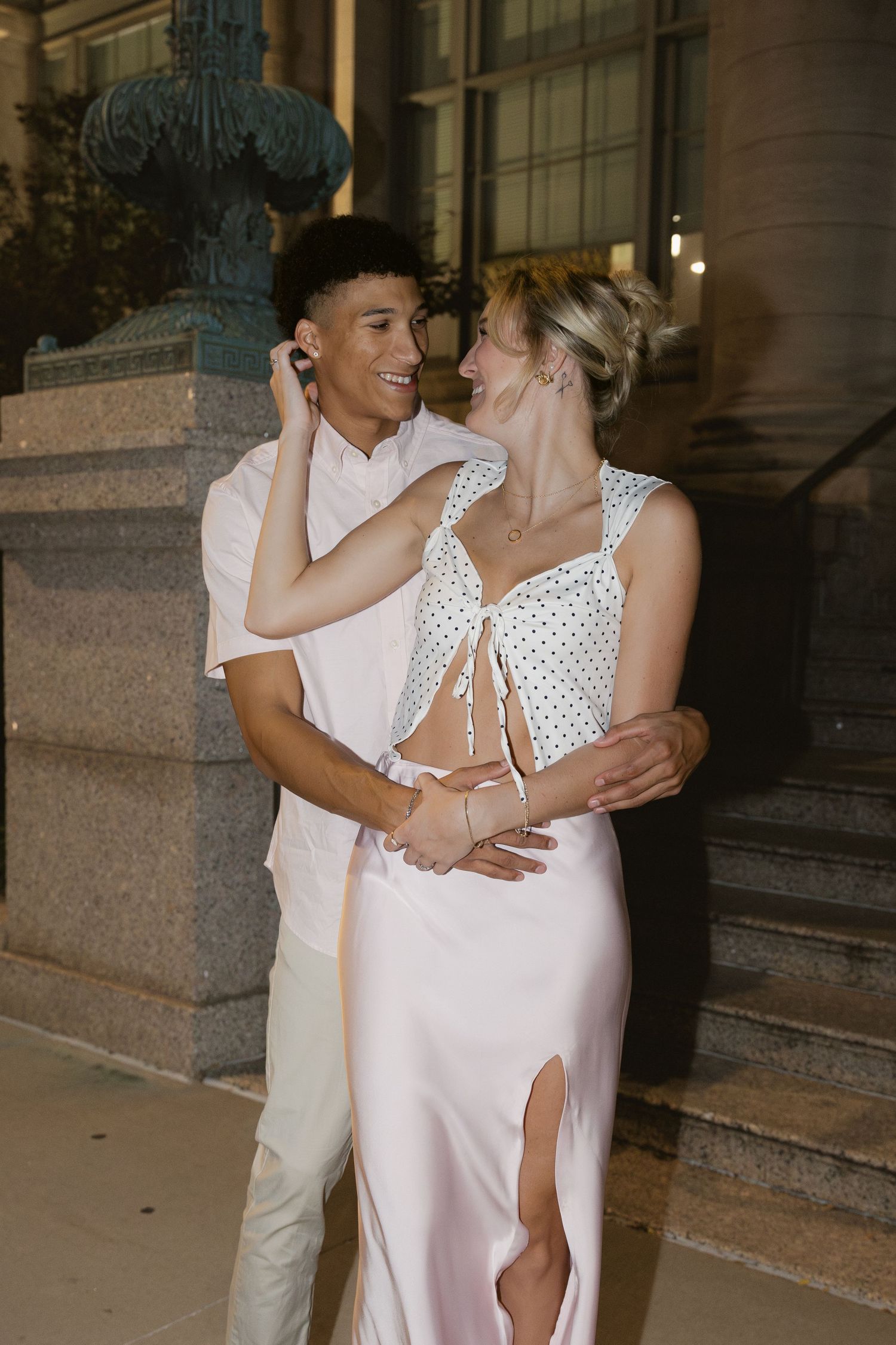 Couple in white outfits sharing intimate moments and embracing on stone steps at dusk.