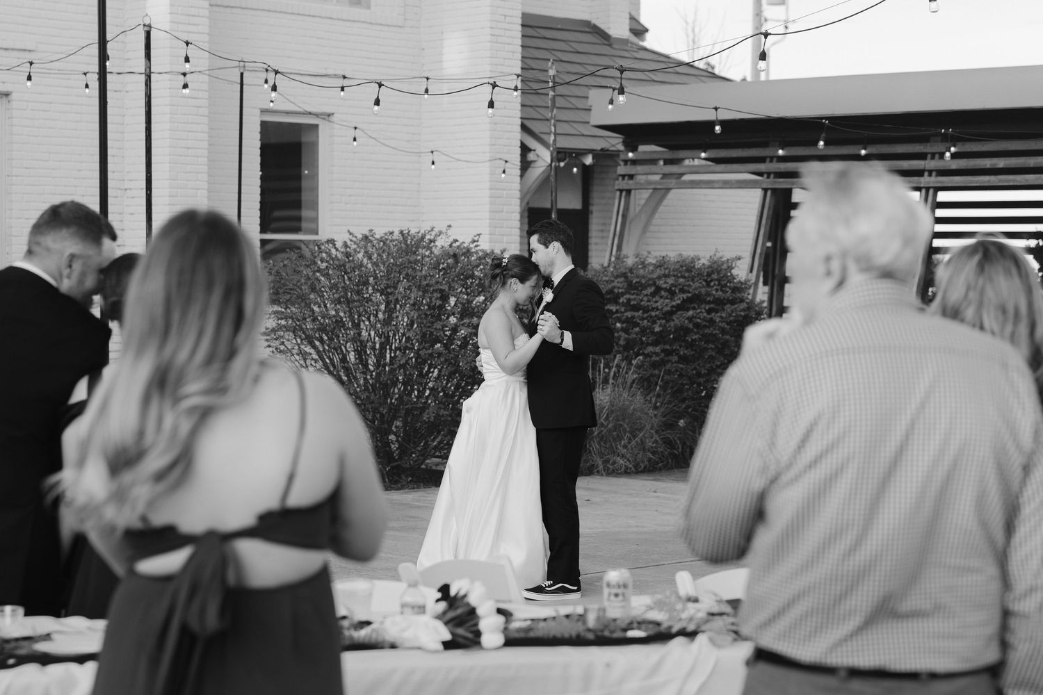 Black and white photo of a bride and groom sharing their first dance at an outdoor wedding reception.