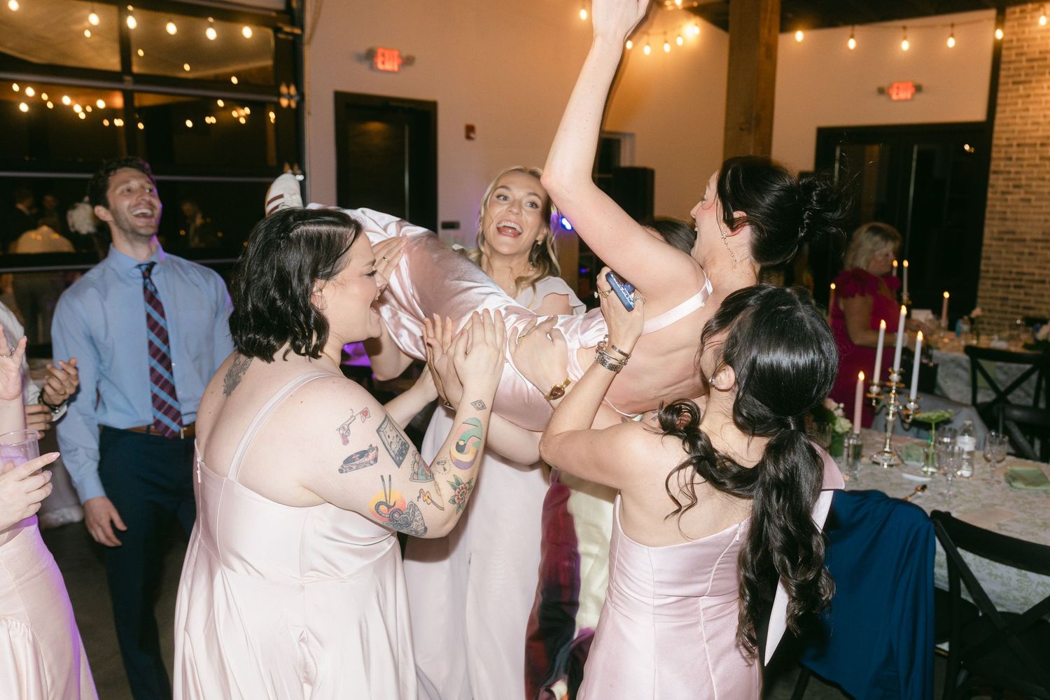 Bridesmaids in blush gowns dancing and celebrating joyfully at wedding reception.