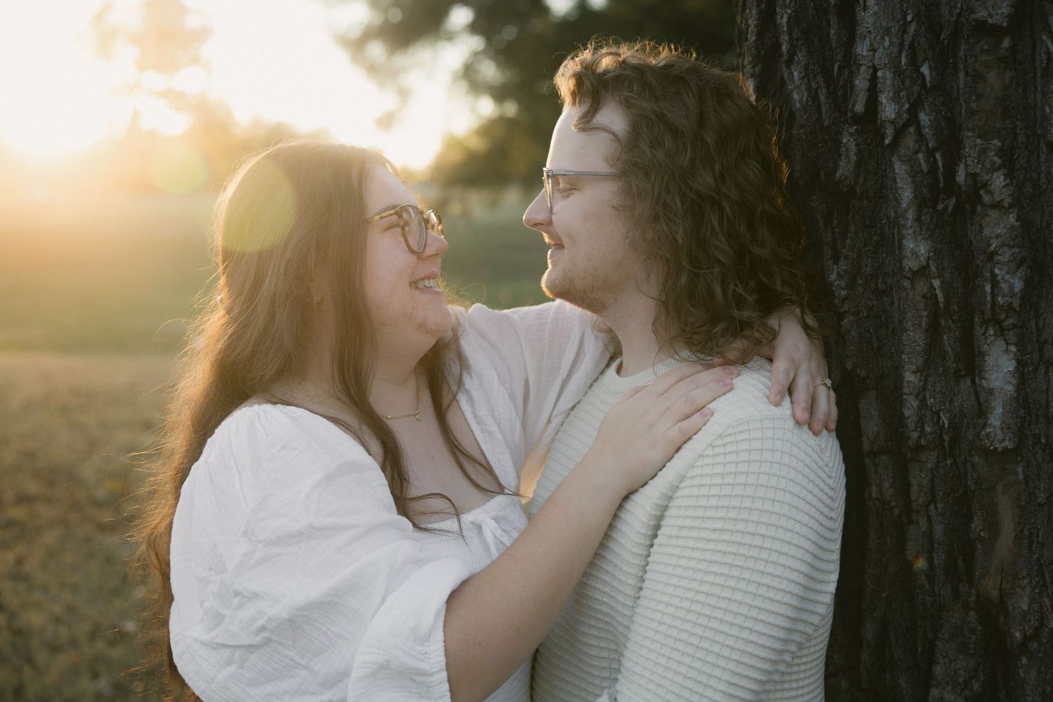 A couple embraces intimately in a sunlit outdoor setting during golden hour with trees in the background.