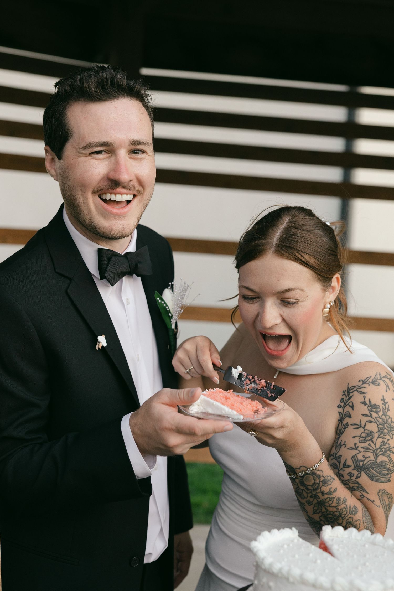 Joyful bride and groom laughing while cutting their wedding cake together at their reception.