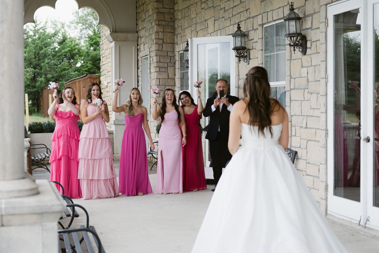 A group in formal attire gathers on a stone porch during a wedding celebration.