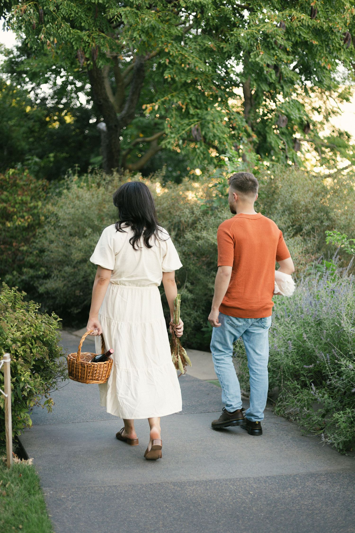 Couple walking together on garden path carrying picnic basket at sunset.