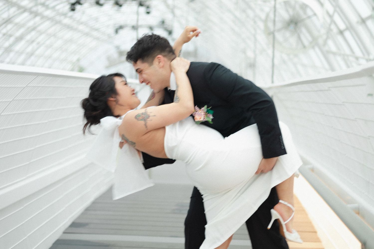 Playful wedding dance dip pose in a bright greenhouse setting.