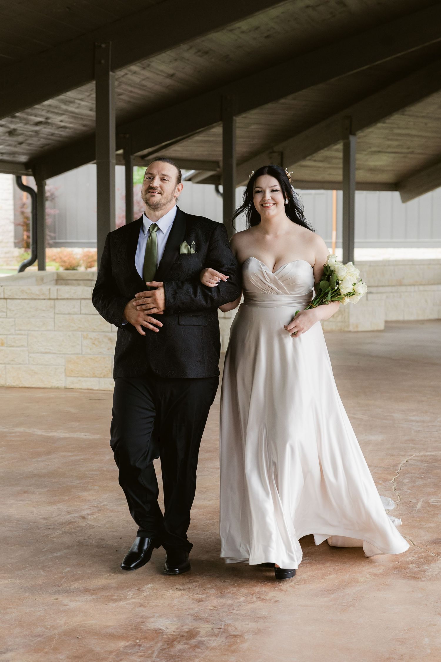 A couple walking down a covered walkway at a wedding venue, with the bride in a flowing white gown.