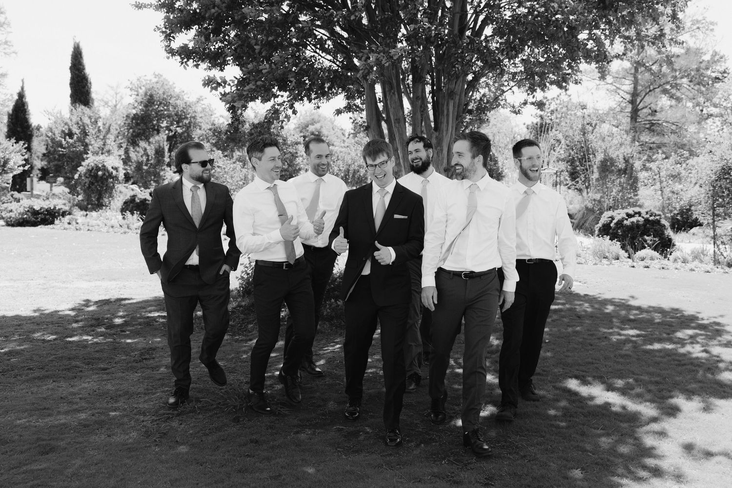 Groom and groomsmen in dark suits walking together outdoors in a classic black and white wedding photo.