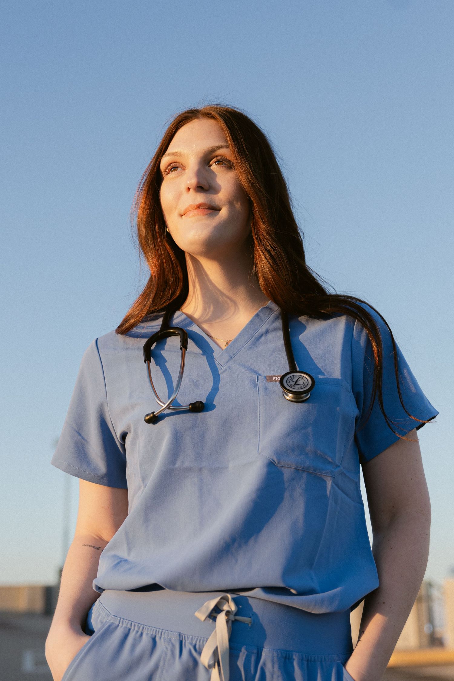 Person in light blue medical scrubs poses in sequence against blue sky at sunset.