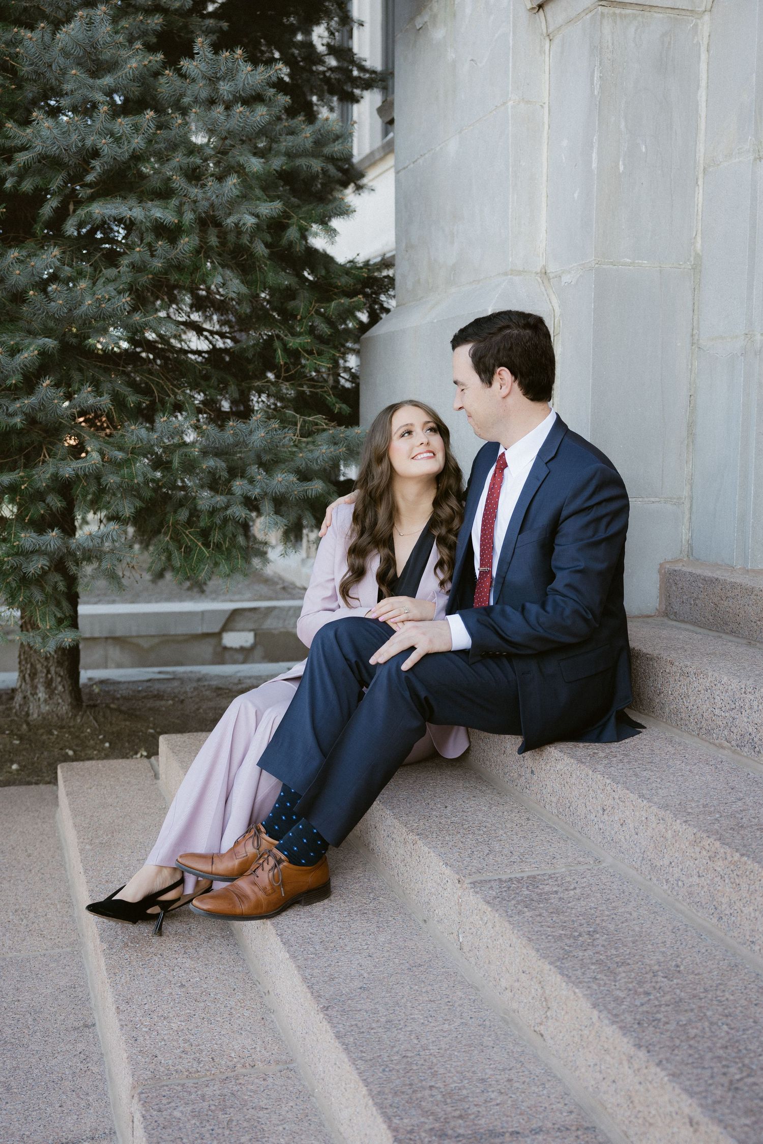 A couple sitting on concrete steps next to a blue spruce tree.