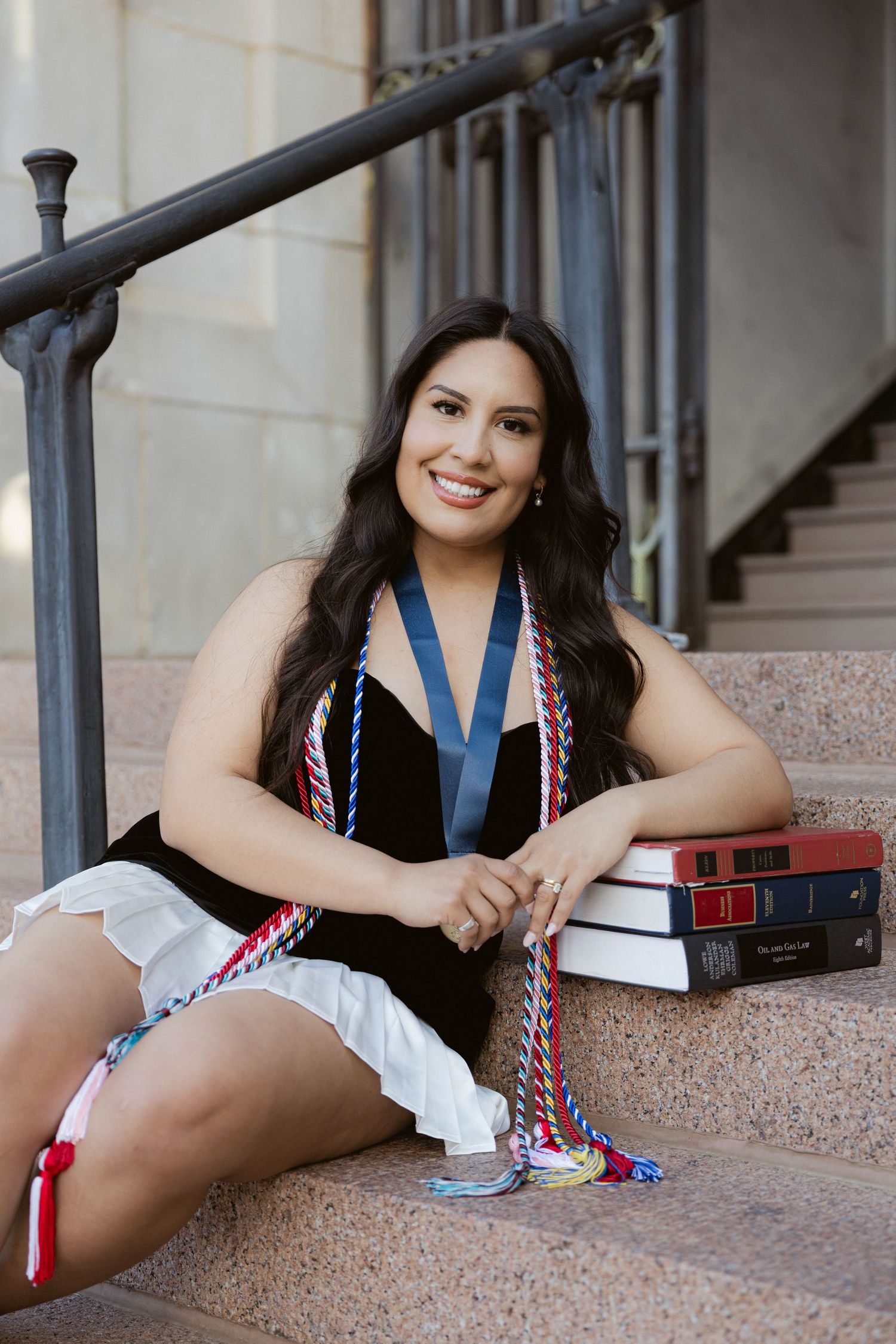 Student in black dress and patriotic braids rests on steps with textbooks in a casual professional pose.