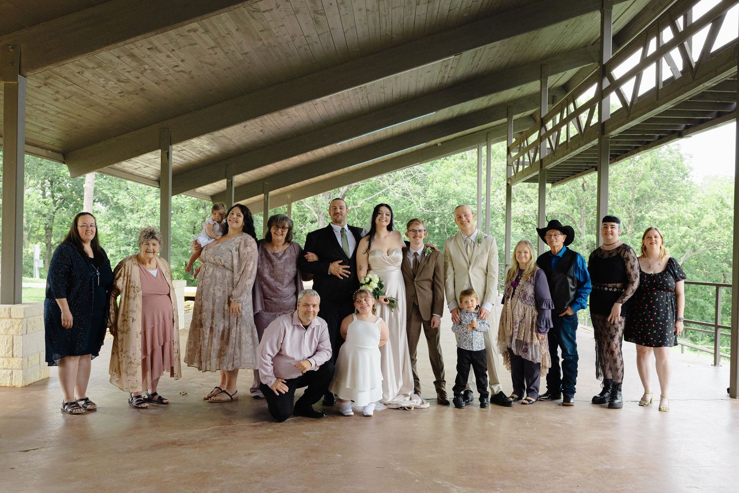 Large group wedding photo of party members lined up on a rustic covered porch.