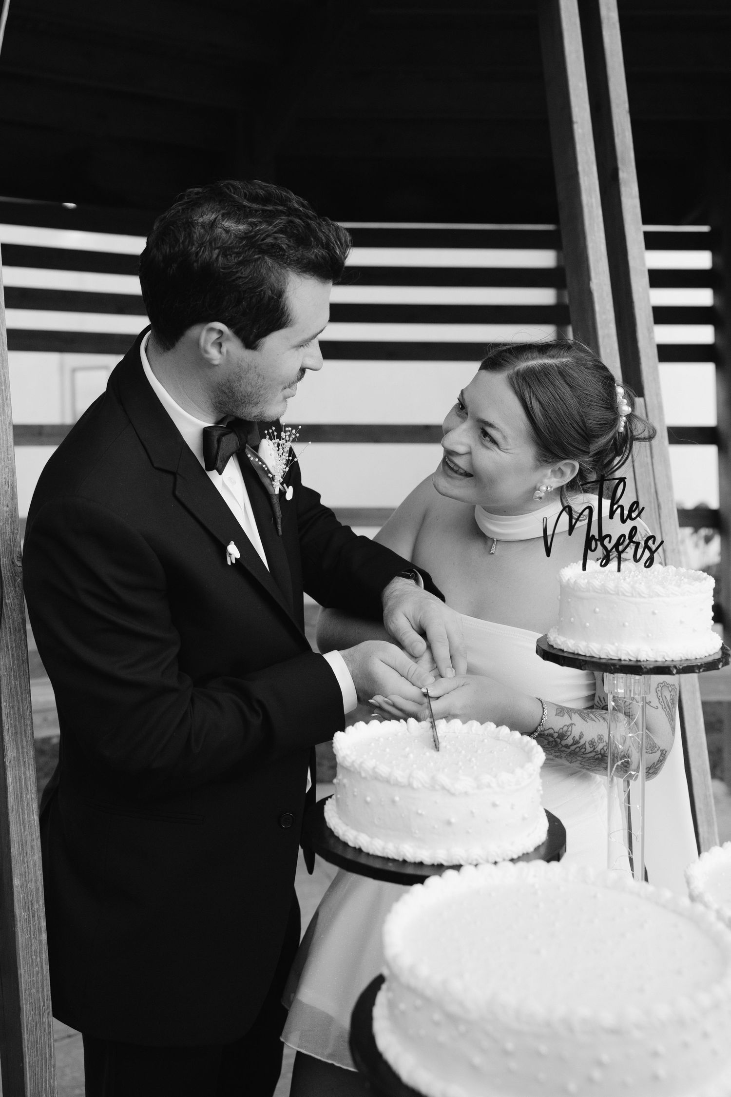 Black and white photo of a bride and groom smiling while cutting their wedding cake together at their reception.