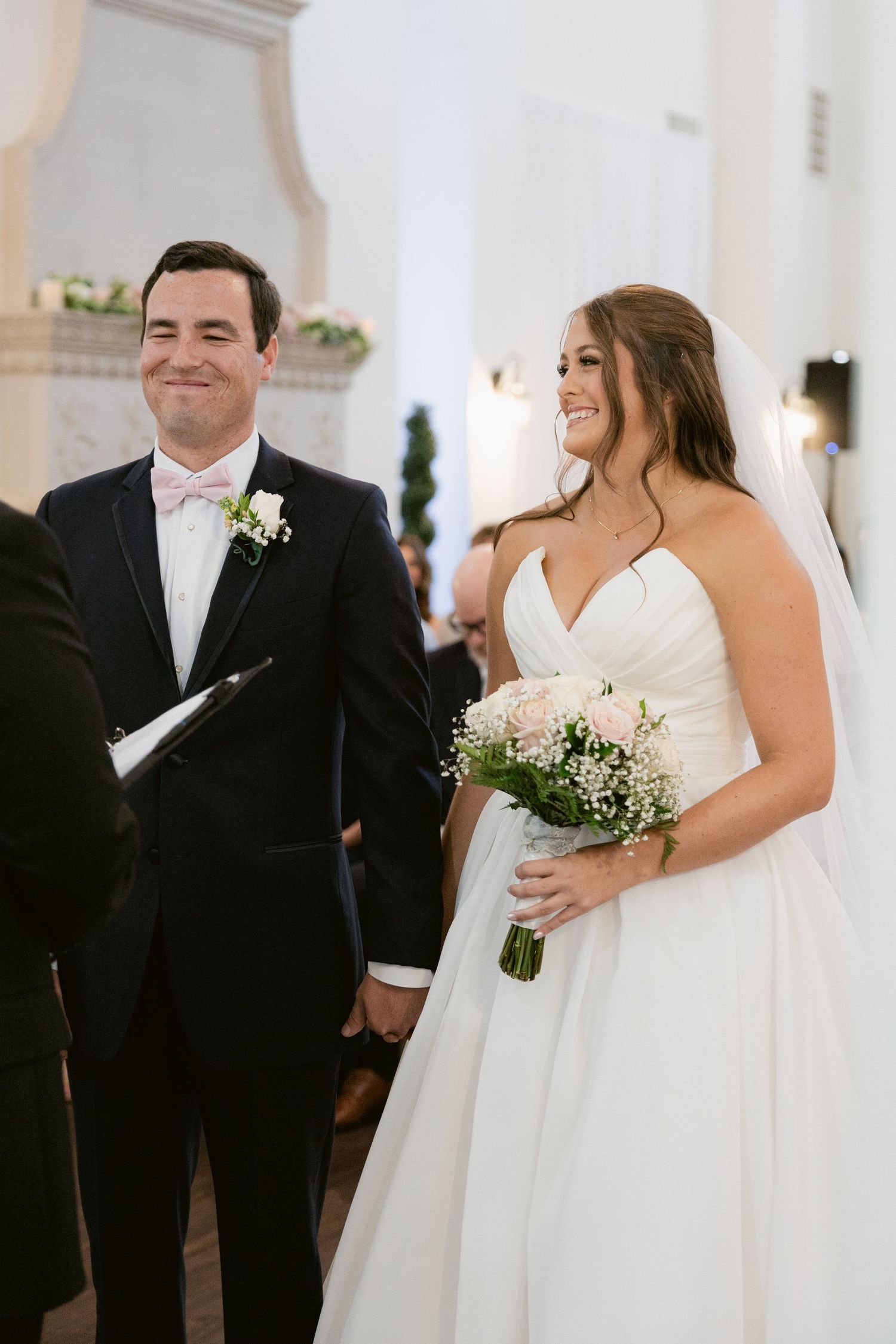 A couple shares a joyful moment during their wedding ceremony in an elegant white chapel.