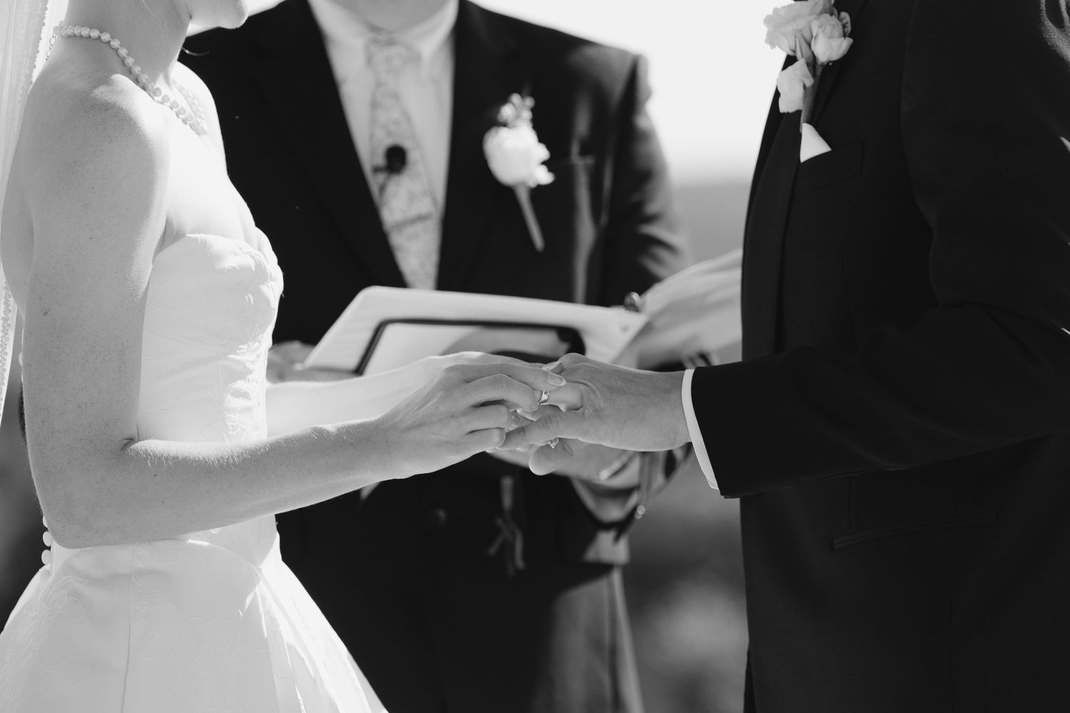 Black and white photo of bride and groom exchanging rings during wedding ceremony.