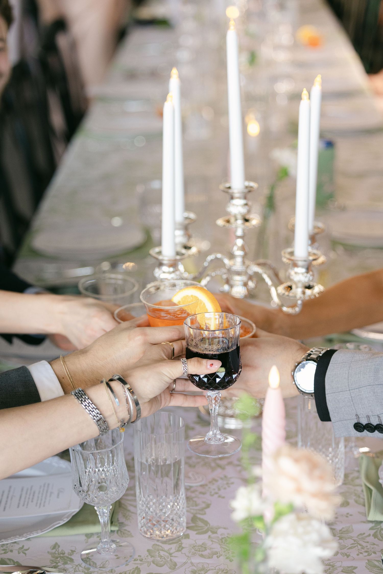 Guests clink glasses in a wedding toast over an elegant candlelit table with silver candelabras and crystal glassware.