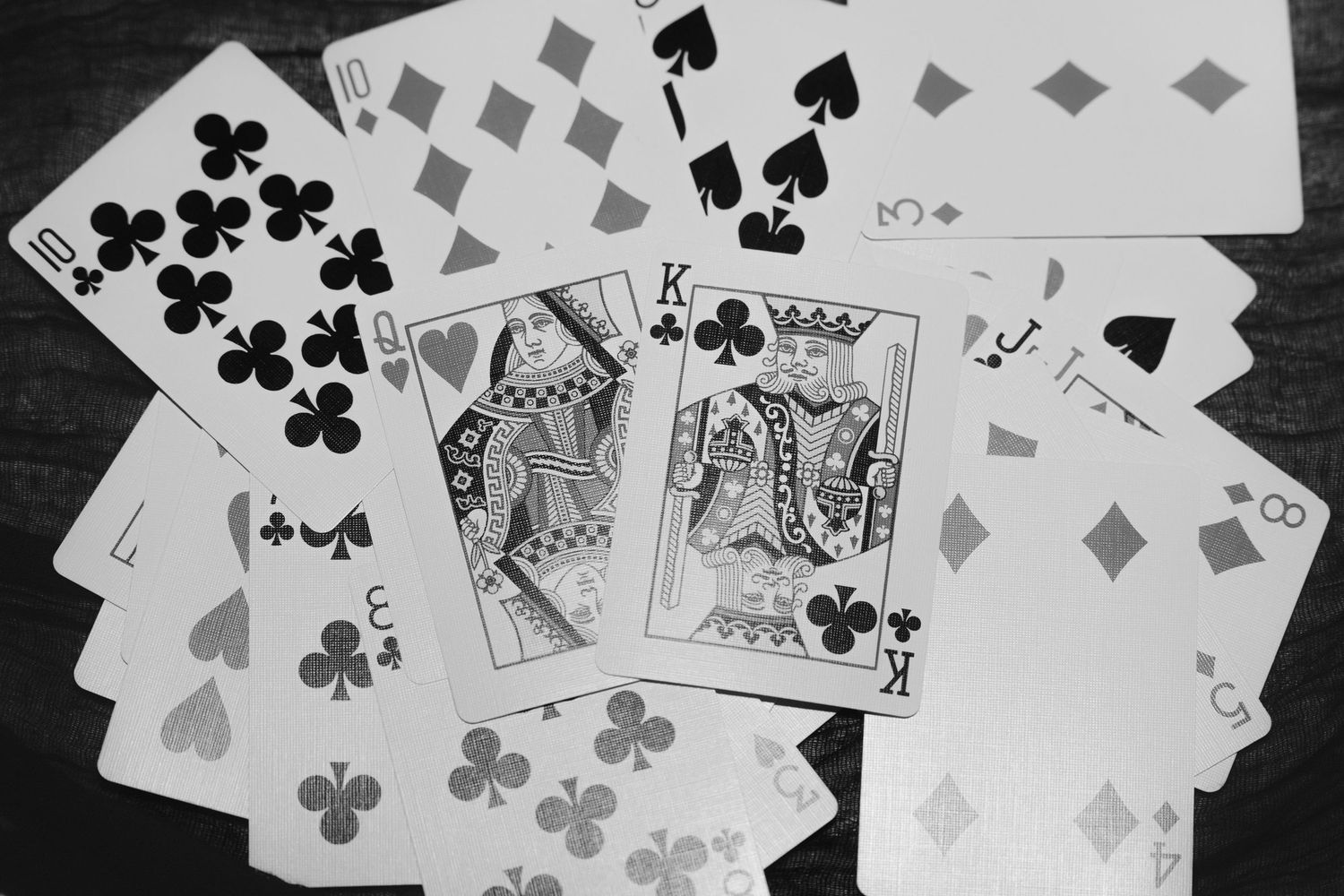Black and white photo of scattered playing cards including a King, Jack, and Ten on a wooden surface.