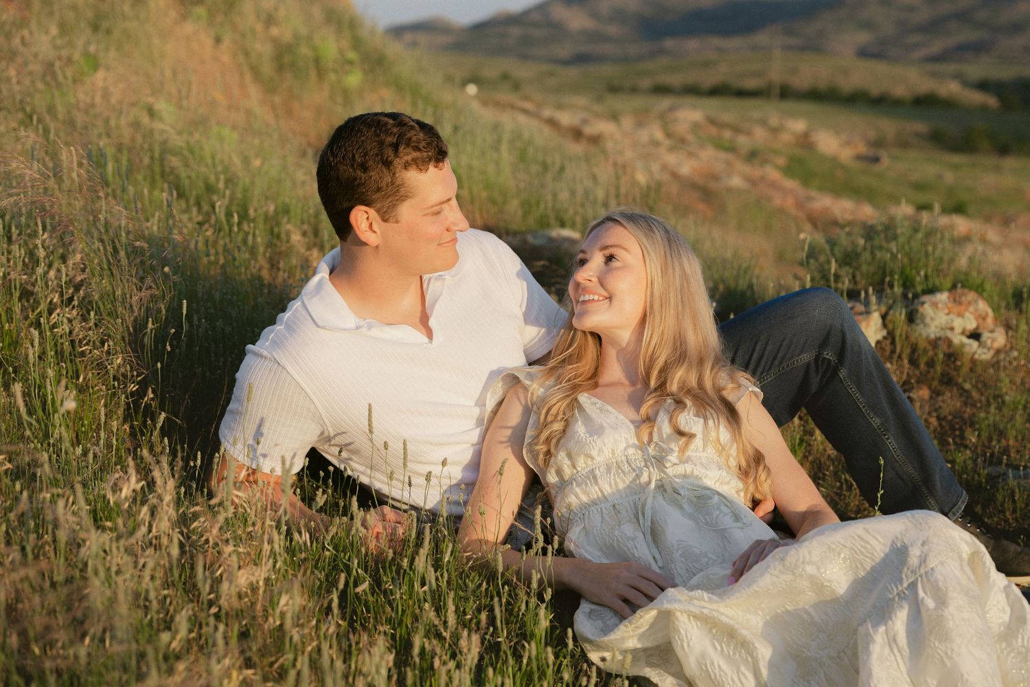 Couple embracing on grassy hillside during golden hour photography session.
