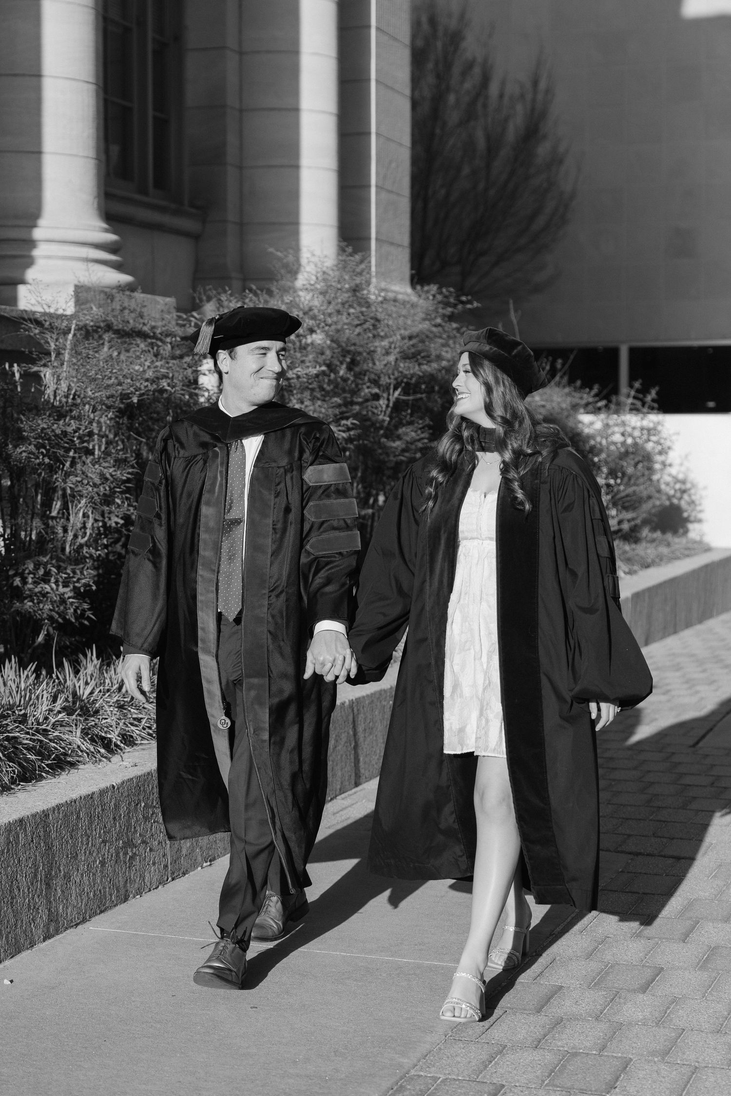 Black and white photo of graduates walking together in academic regalia outside a building.