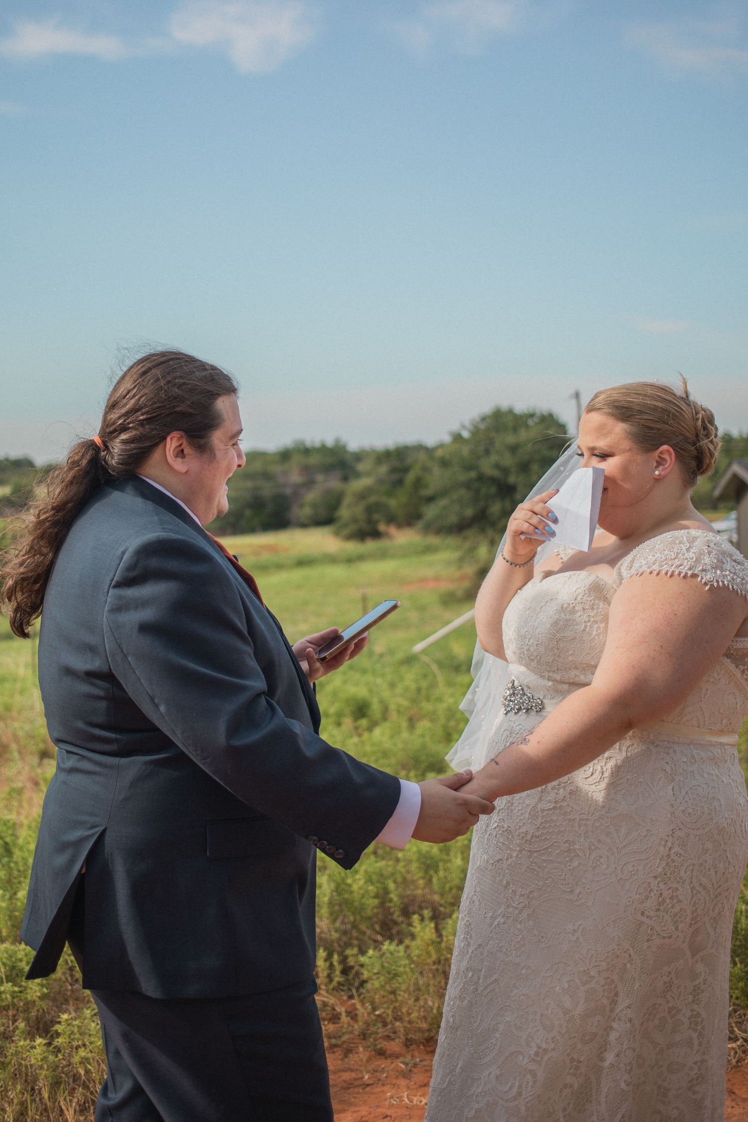 Wedding ceremony taking place outdoors in a field on a sunny day showing emotional exchange of vows.