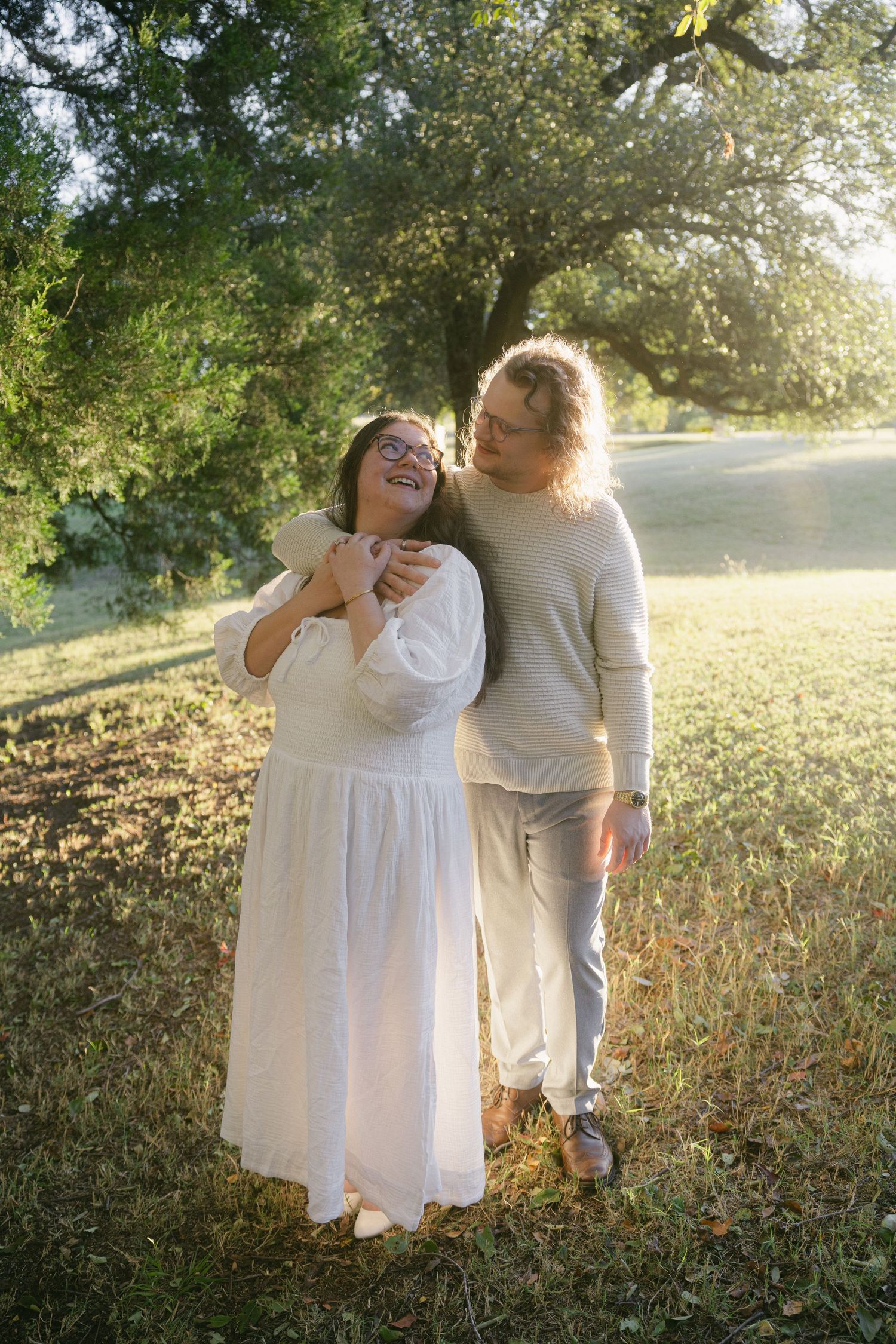 Two people in white outfits share a tender moment together in a sunlit field at golden hour.