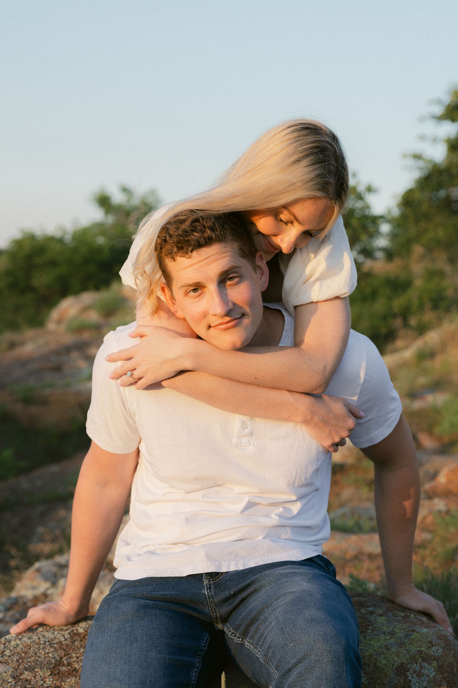A romantic couple sits together on rocky terrain at sunset sharing tender embraces and playful moments.