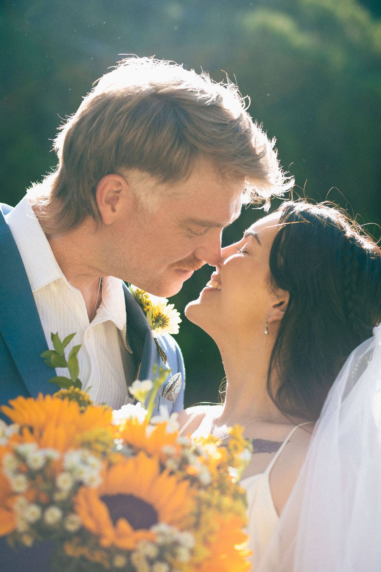 A romantic wedding couple shares an intimate moment in golden sunlight with orange sunflowers in the foreground.