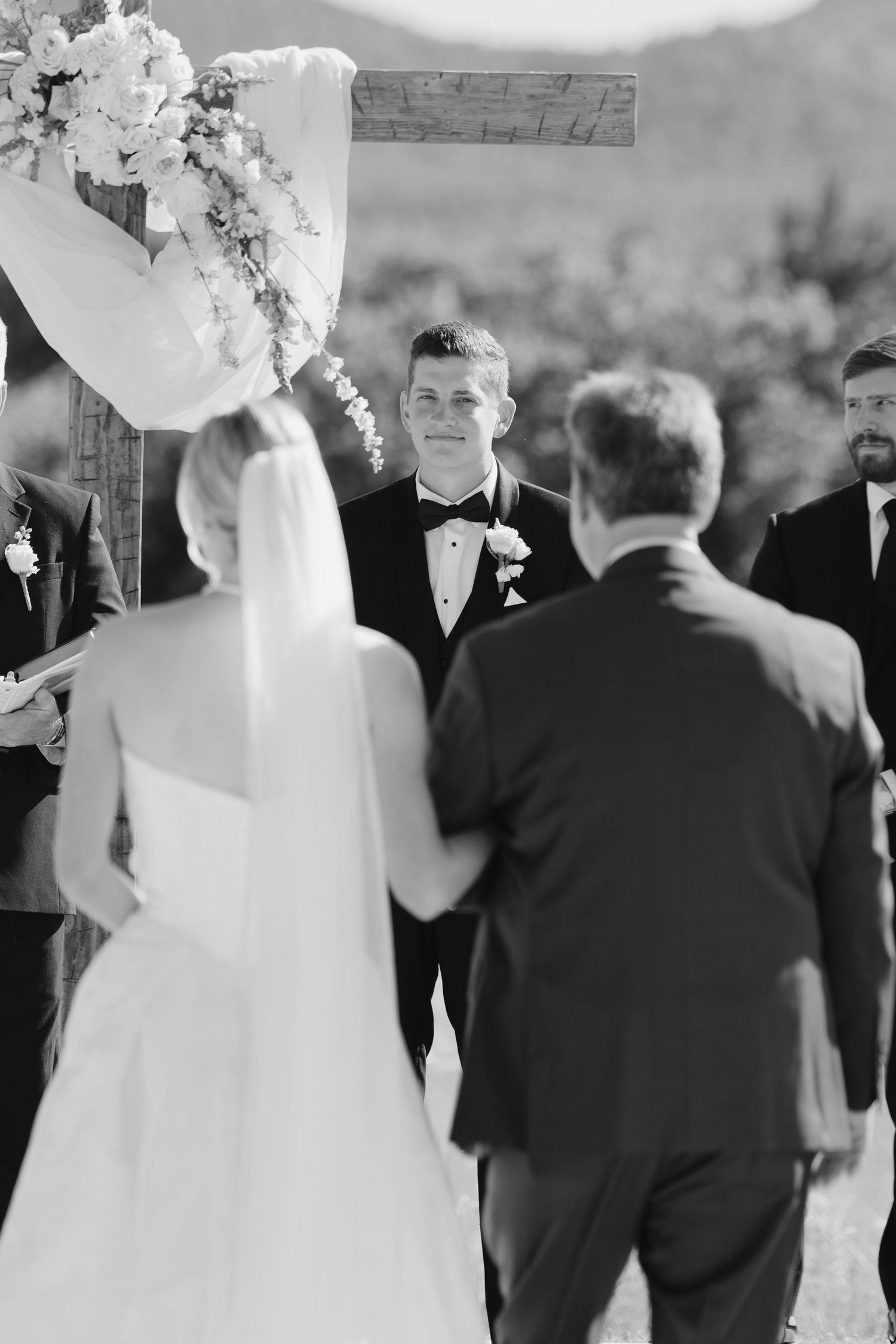 Groom smiling at bride during outdoor wedding ceremony in black and white photography.