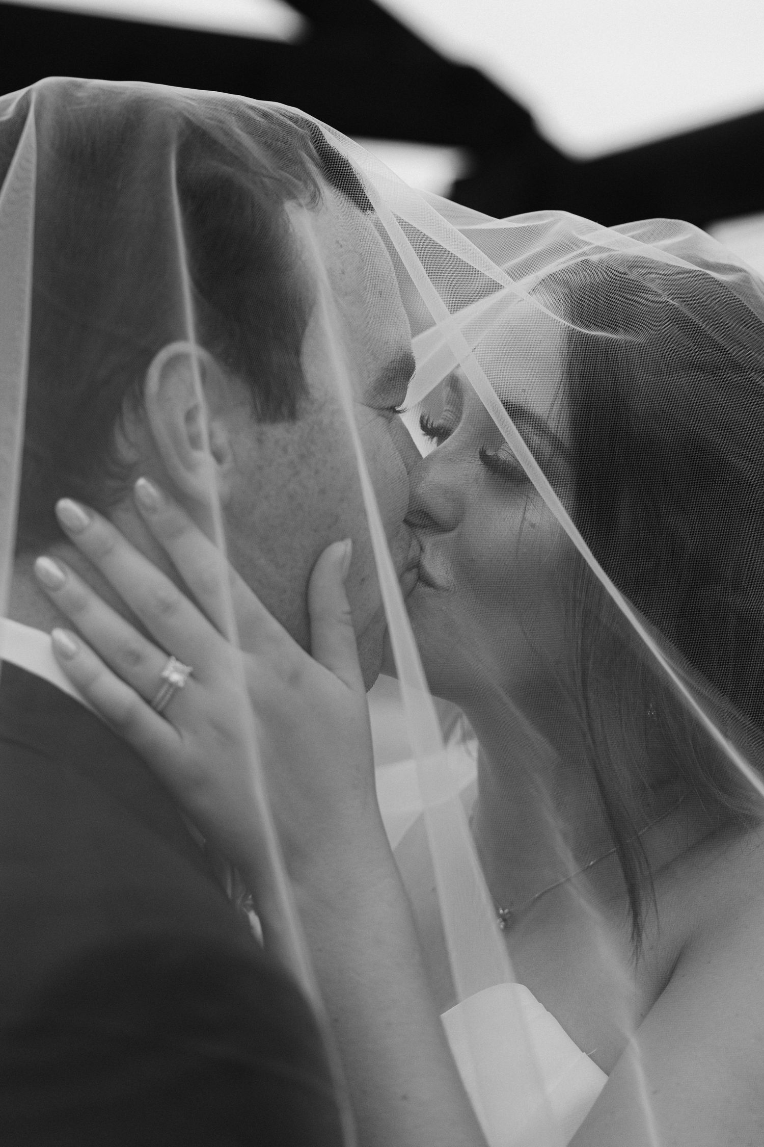 A romantic sequence of wedding kisses through a delicate white veil, shown in black and white.