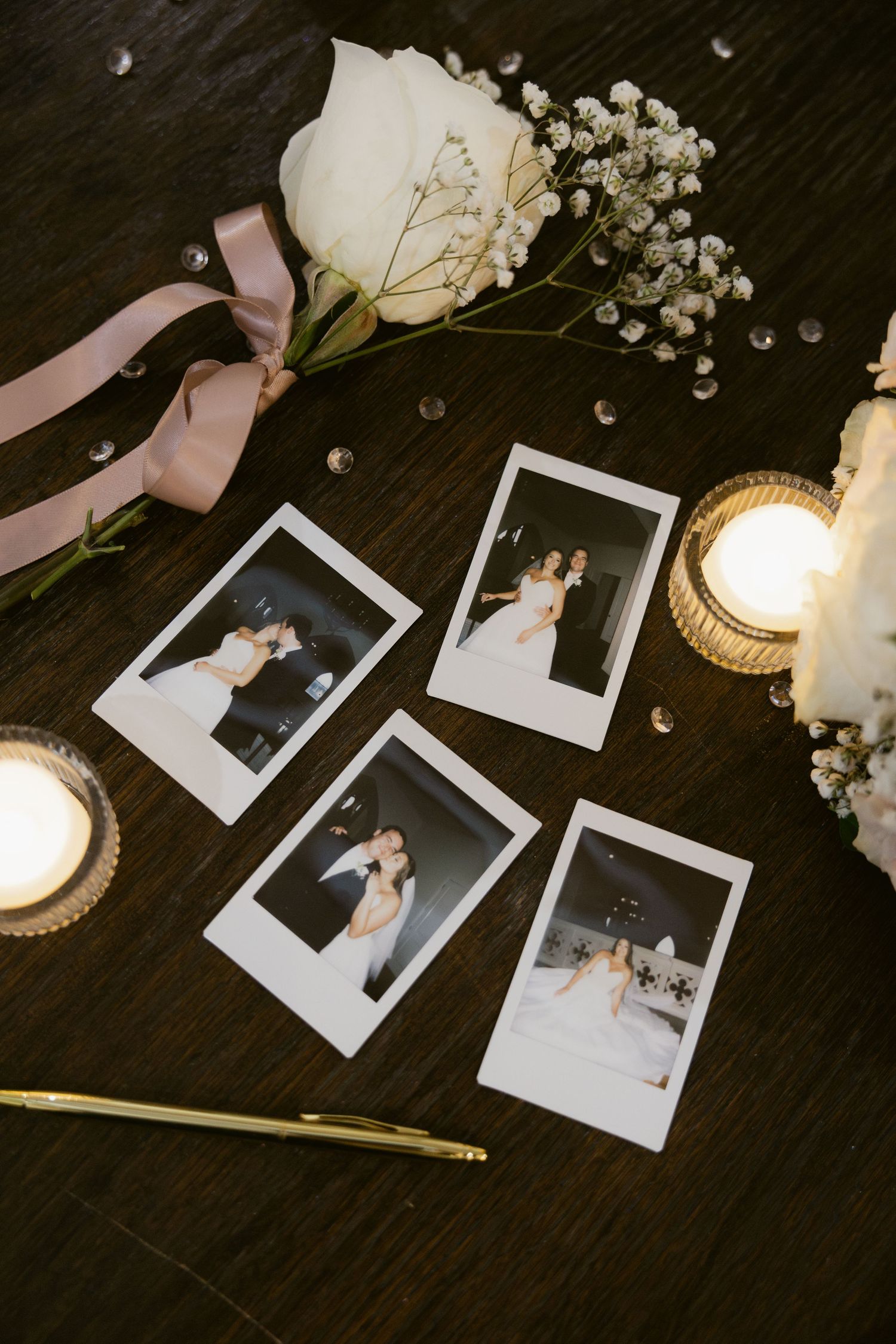 Polaroid photos arranged with delicate baby's breath flowers and a lit candle on a dark wooden surface.
