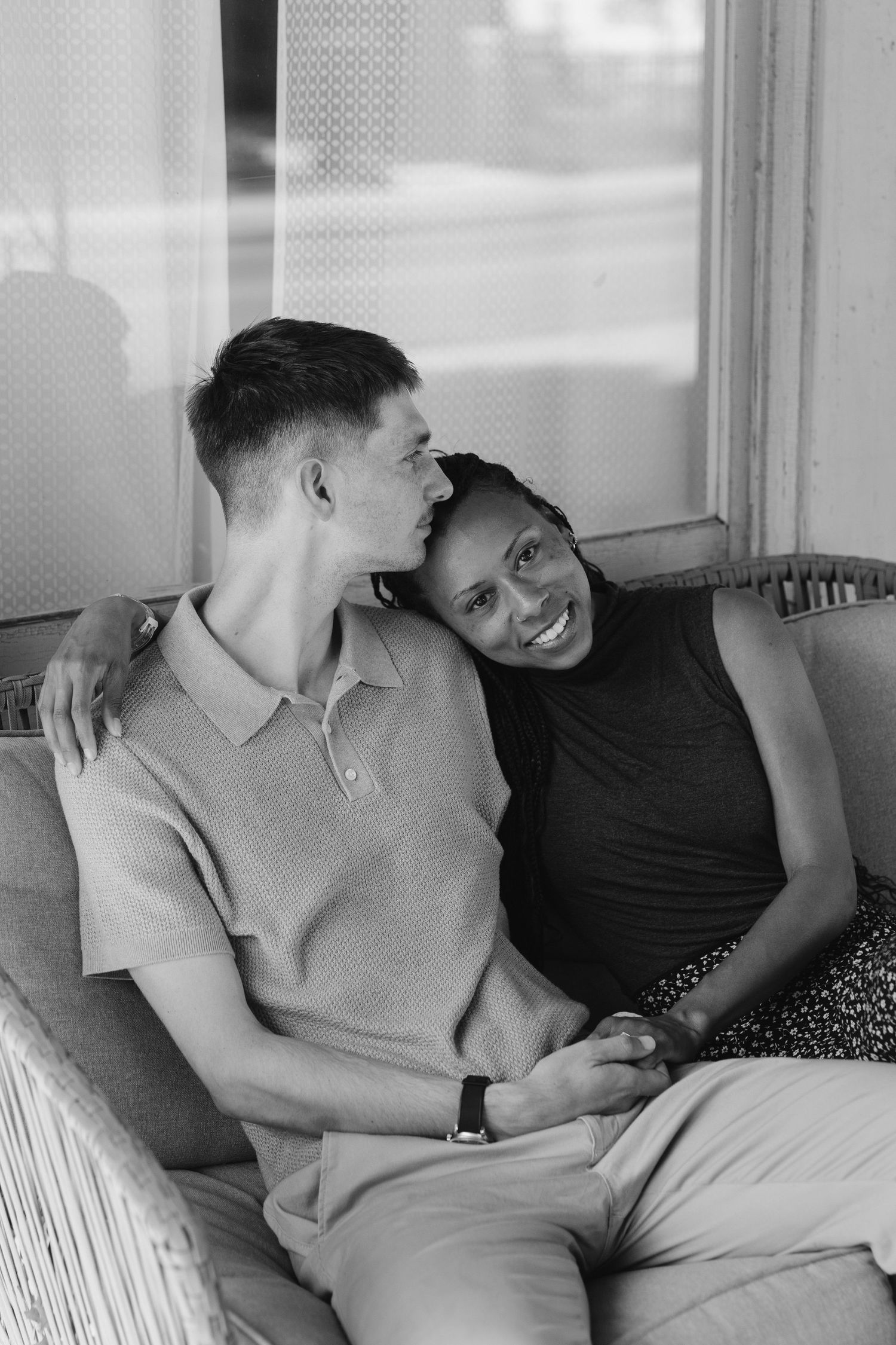 Black and white photo of a smiling interracial couple relaxing together on a couch, woman leaning on mans shoulder.