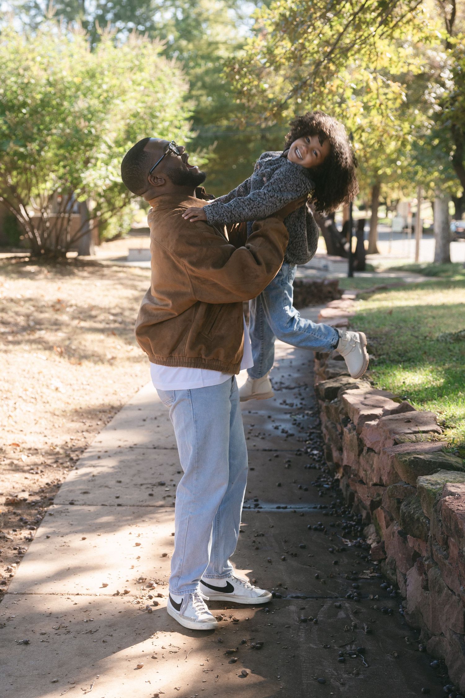 A person in jeans and brown jacket climbs over a stone wall in a park on a sunny autumn day.
