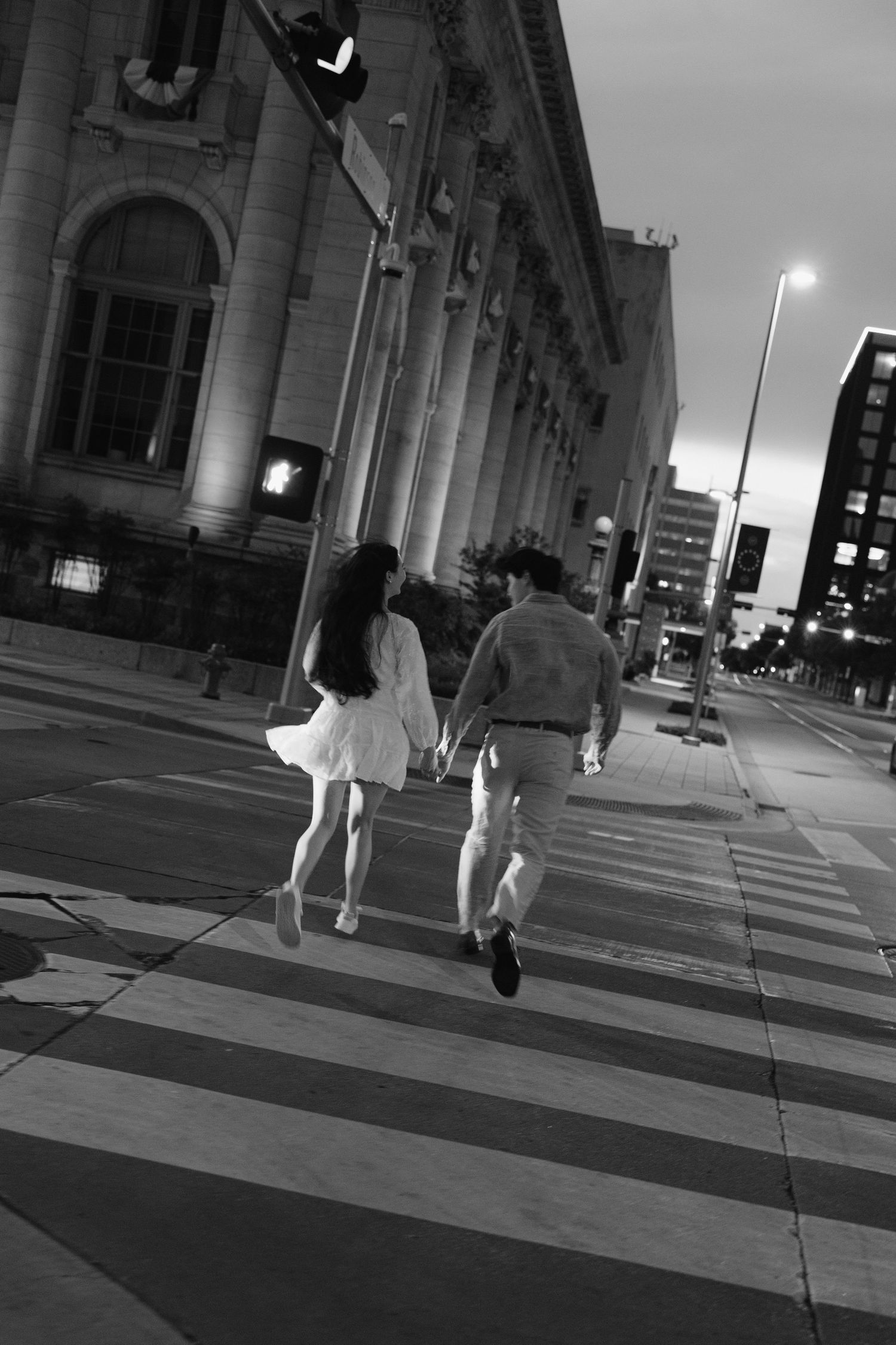 Couple holding hands crossing street at night in black and white urban photo.