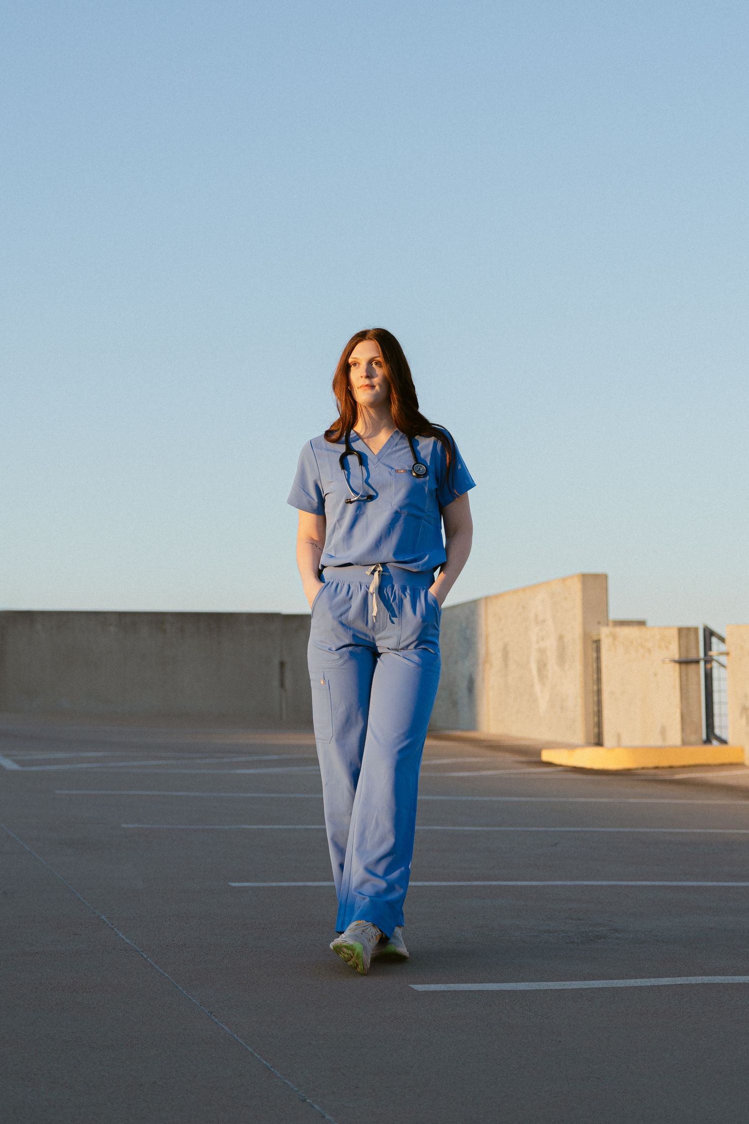 Sequence of shots showing a person in blue scrubs walking and turning on an empty rooftop parking area at sunset.