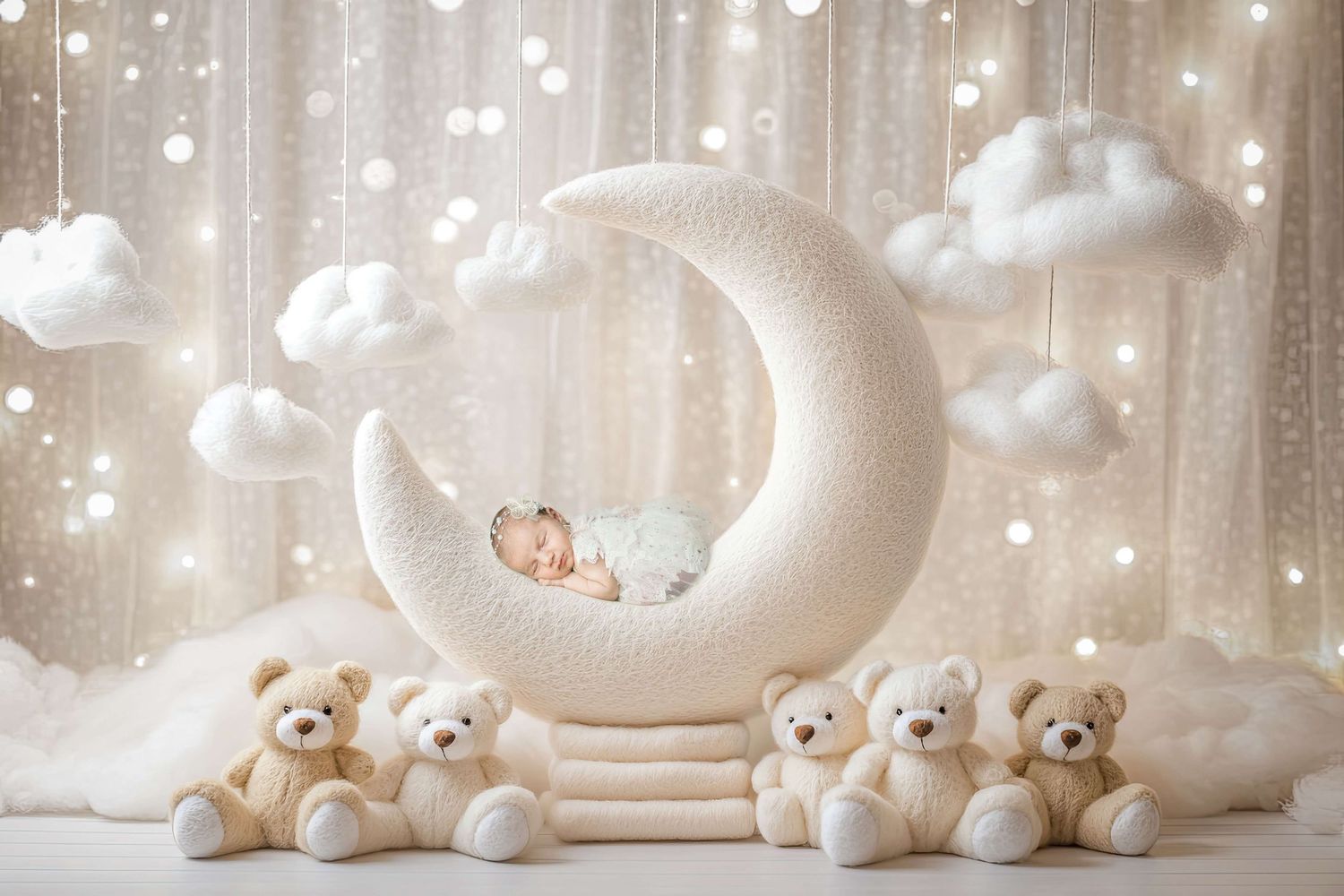 Newborn baby sleeping on a white crescent moon prop surrounded by teddy bears and fluffy clouds in a dreamy studio setup.