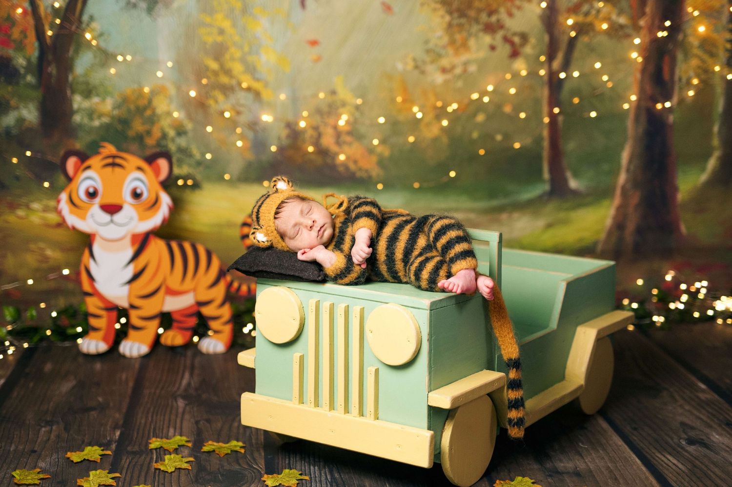 Sleeping newborn in tiger costume inside a miniature green jeep toy beside a tiger figurine on a woodland backdrop.