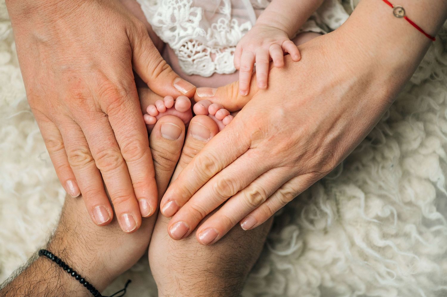 Parents and newborn baby feet held together in loving hands on a soft white fur blanket, family bonding moment.
