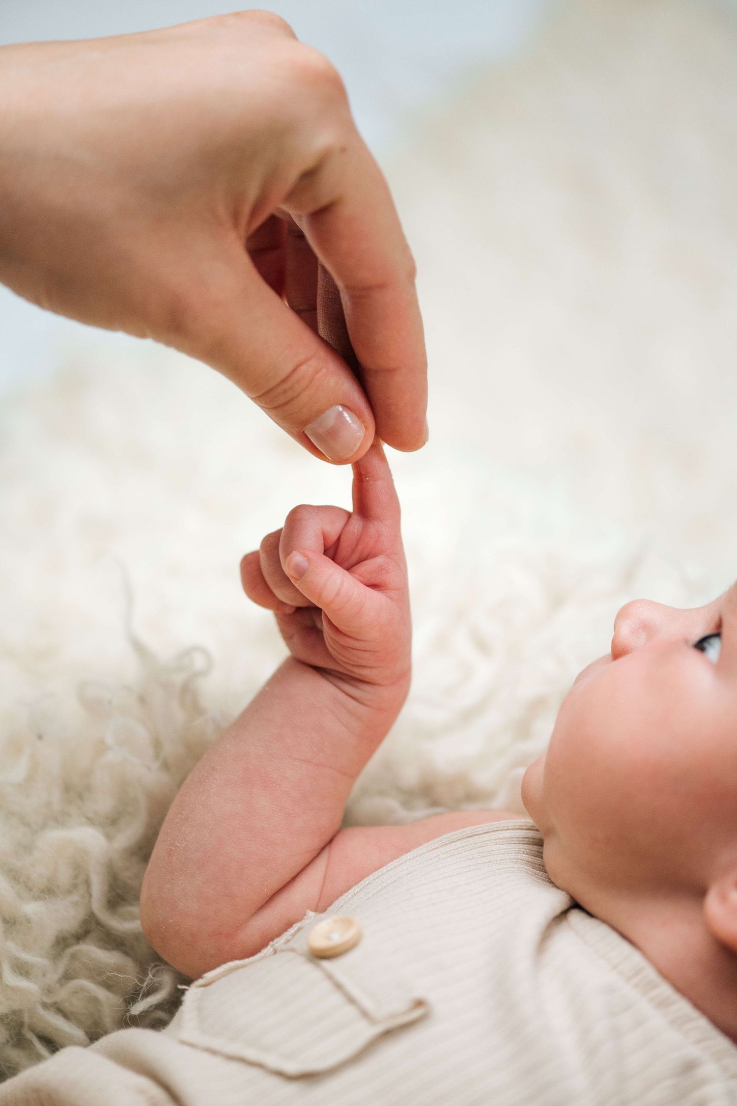 Newborn baby grasping adult finger while lying on soft white fluffy blanket, close-up of tiny hand and fingers.