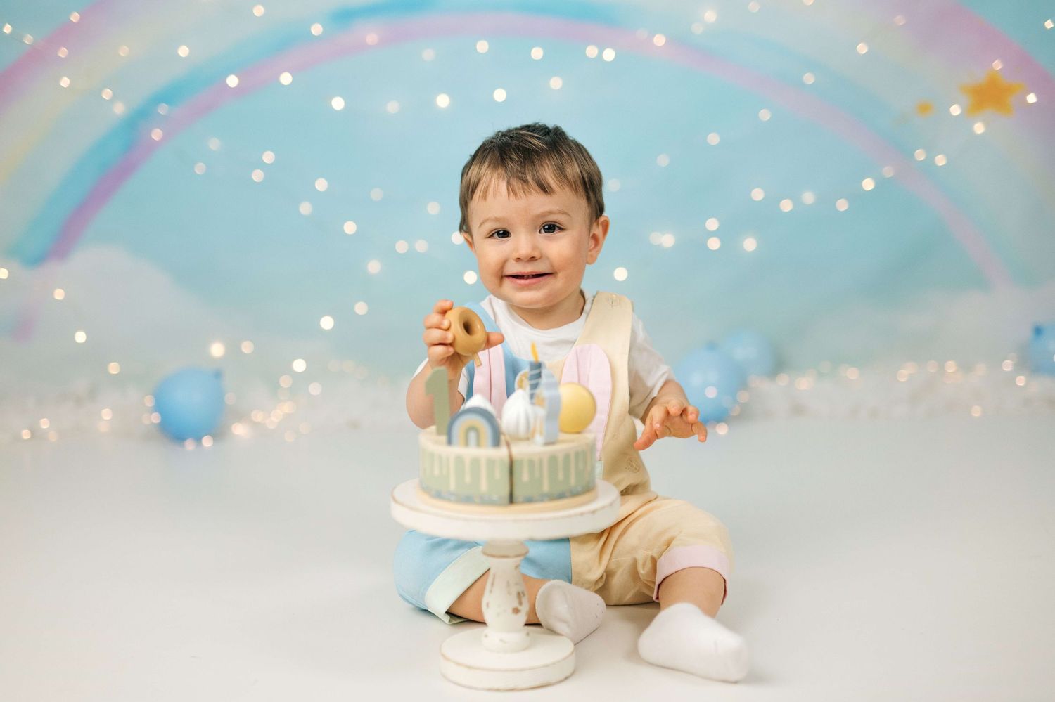 Smiling baby boy sitting with a pastel blue birthday cake during a first birthday cake smash photo session.