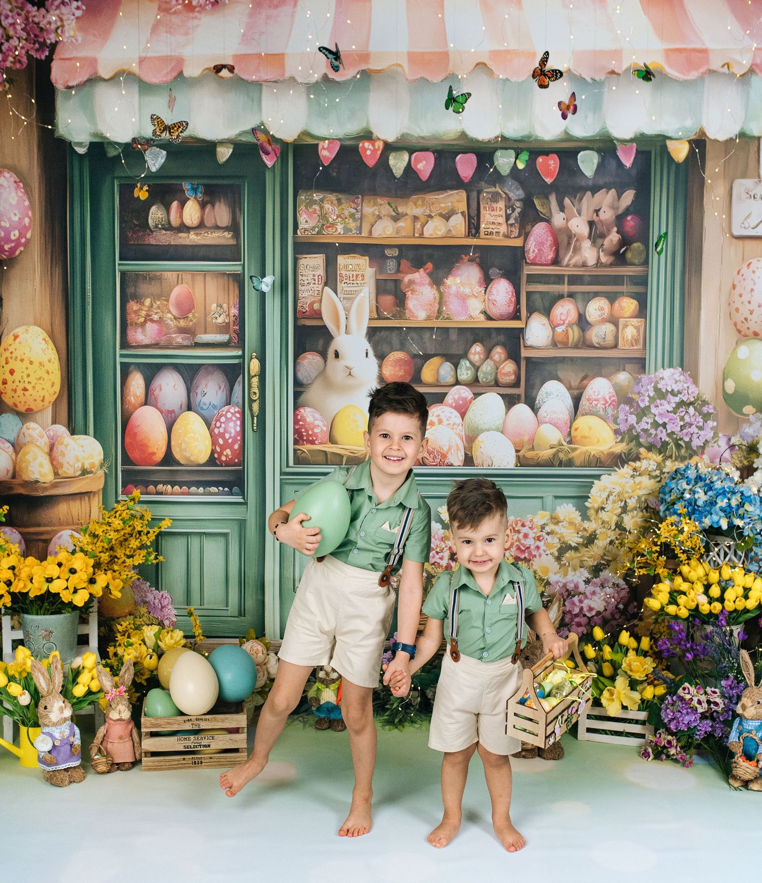 Two boys in green shirts pose before a colorful Easter egg shop backdrop with bunnies, flowers, and decorated eggs.