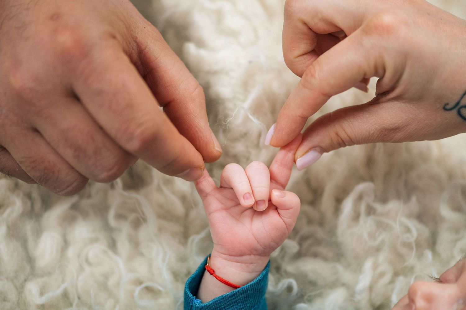 Newborn baby gripping parents fingers on a soft white fluffy blanket background.