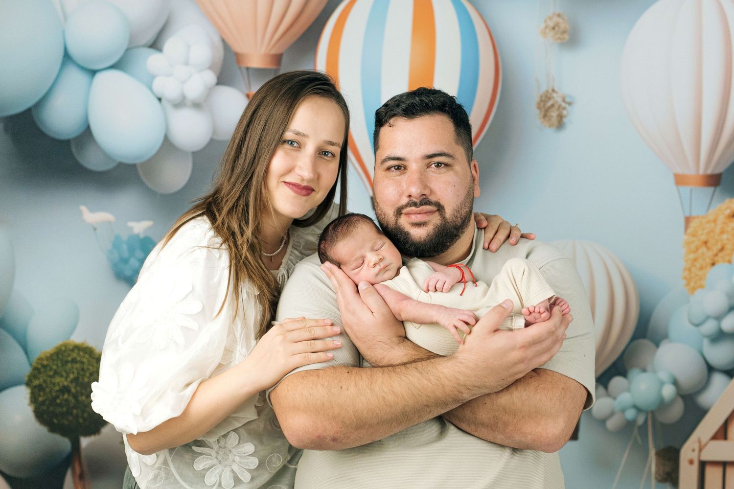 Happy parents pose with their sleeping newborn baby in a whimsical hot air balloon themed photo.