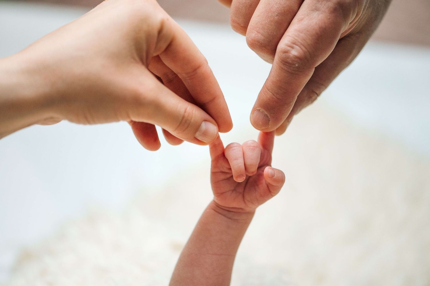 Two adult hands gently touching a newborn baby's tiny hand, symbolizing family love and new parenthood.