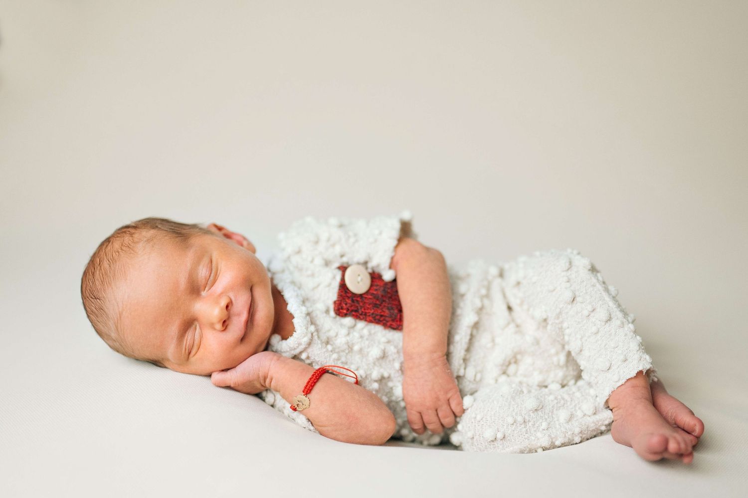 Sleeping newborn baby wrapped in white knit blanket wearing red Santa hat for Christmas portrait.