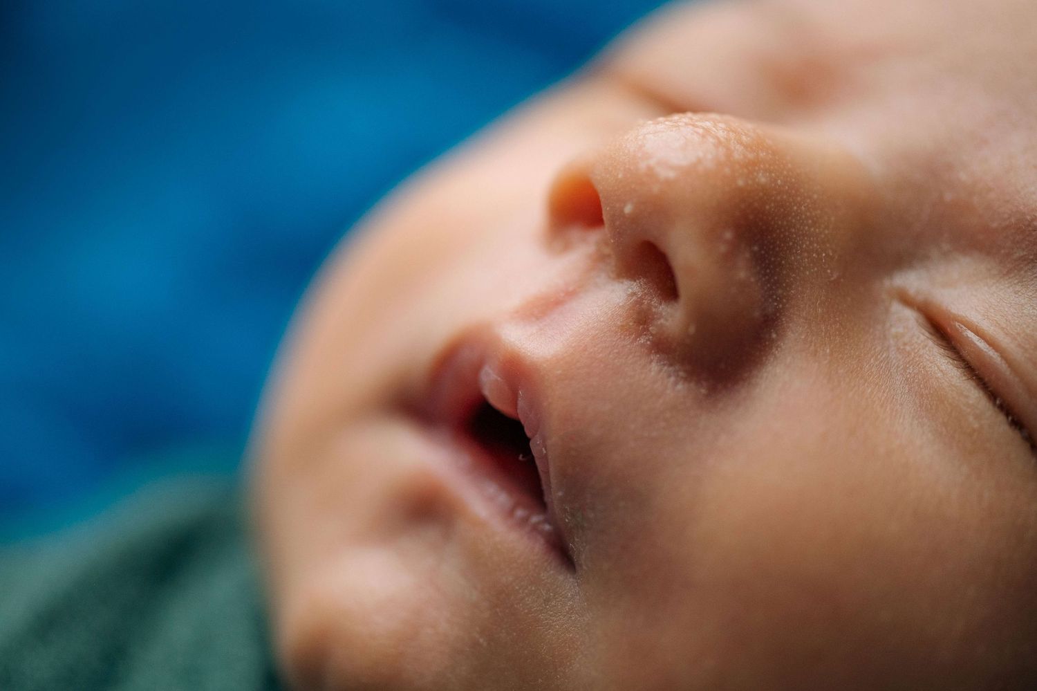 Close-up of a sleeping newborn baby with delicate features resting on a blue background.