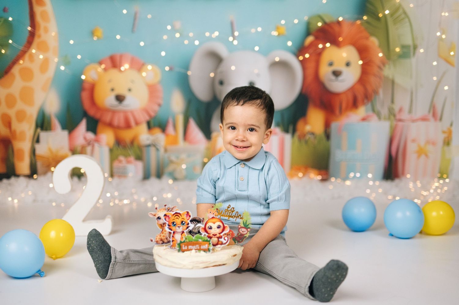 Smiling baby boy sits with safari animal cake at first birthday cake smash with colorful jungle backdrop.