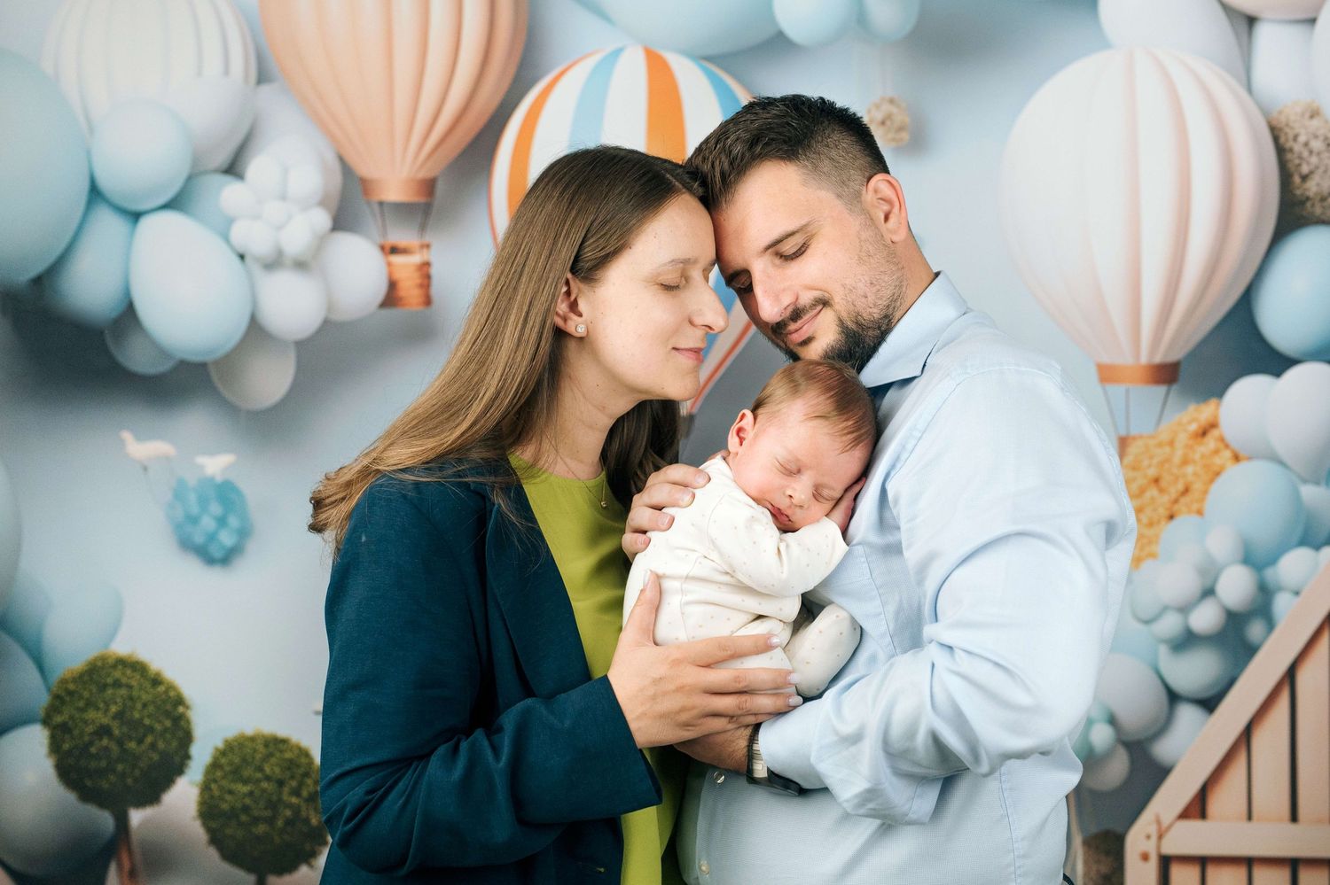 Parents tenderly hold their newborn baby in a dreamy blue balloon-themed photo studio backdrop.