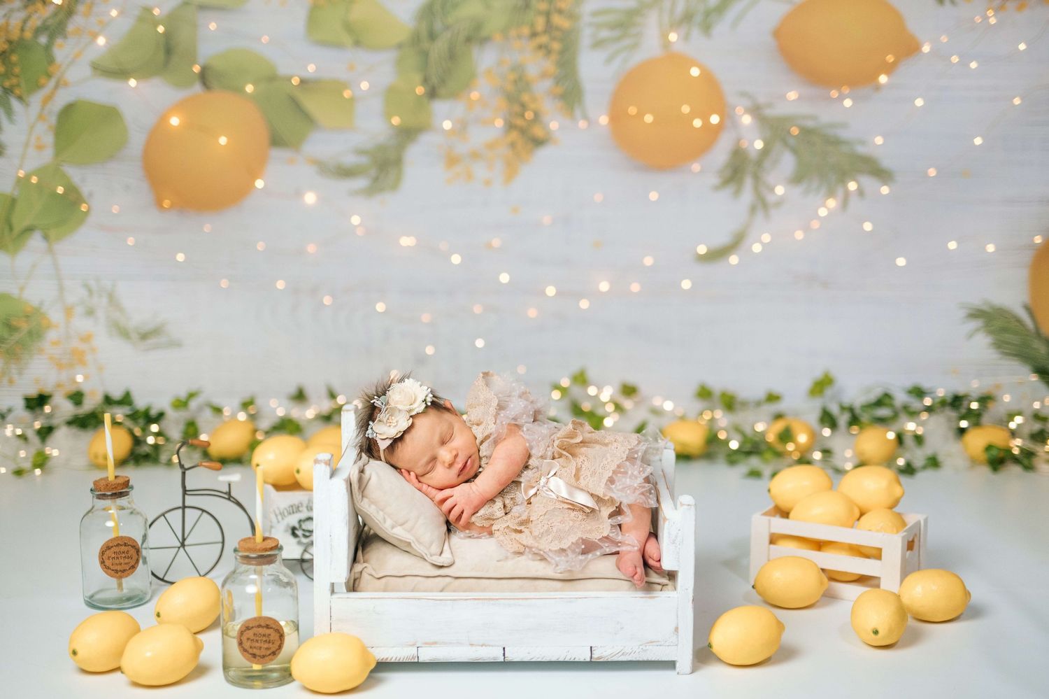 Newborn baby sleeping on white miniature bed surrounded by lemons and fairy lights in a whimsical lemon-themed photo setup.