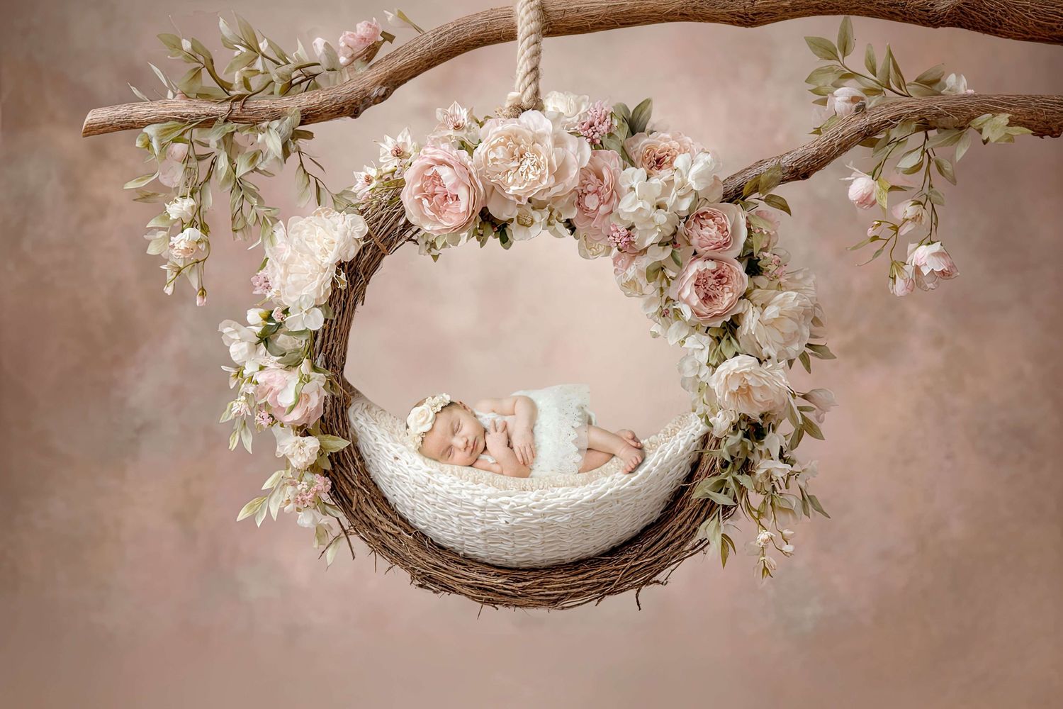Newborn baby sleeping peacefully in a floral wreath swing adorned with pink roses, hanging from a rustic branch.